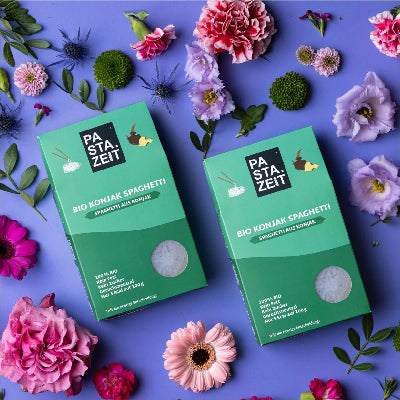 Zwei Konjak Spaghetti Verpackungen von Pastazeit auf einem violetten Hintergrund mit Blumen