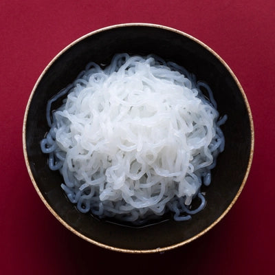 Konjak Spaghetti ohne Sauce in einer schwarzen Schüssel auf roten Hintergrund