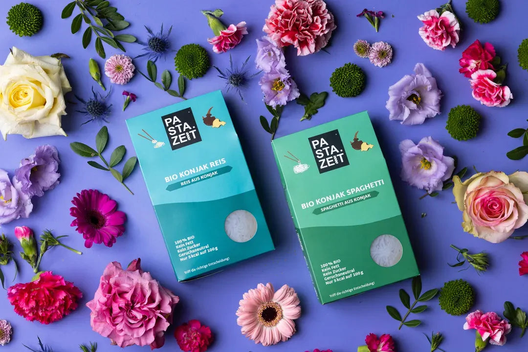 Packungen Bio Konjak Nudeln und Konjak Spaghetti umgeben von bunten Blumen