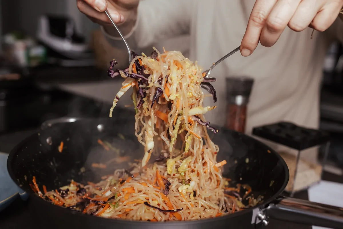 Wok-Nudeln mit Gemüse werden mit Stäbchen aus der Pfanne gehoben