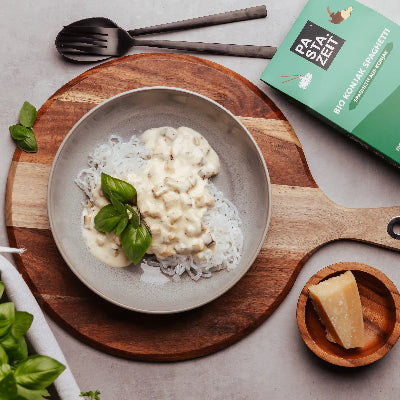 Konjak Spaghetti von Pastazeit mit veganer Carbonara Sauce auf einem Teller angerichtet. Rundherum liegen Zutaten und Besteck