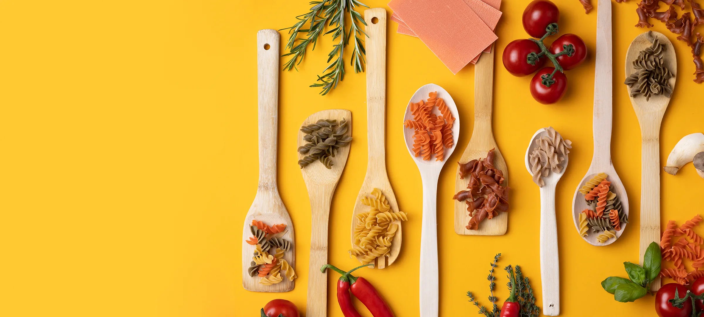 Kochlöffel mit bunten Bio-Fusilli aus Linsen, Erbsen und Kichererbsen auf gelbem Hintergrund